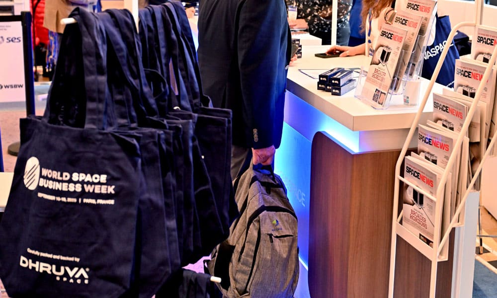 comptoir de réception avec différents objets portant le logo de la World Sapace Business Week et de sponsors